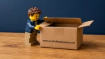 Image of a LEGO style minifigure opening a carboard box